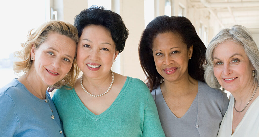 four women side by side smiling in support of Breast cancer awareness and health and wellness month