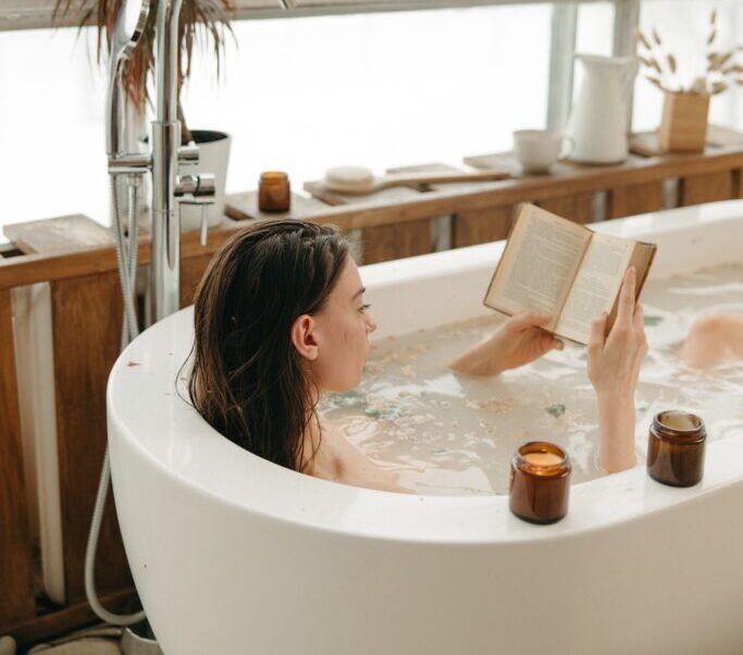 a women in the bathtub reading a book with candles around her