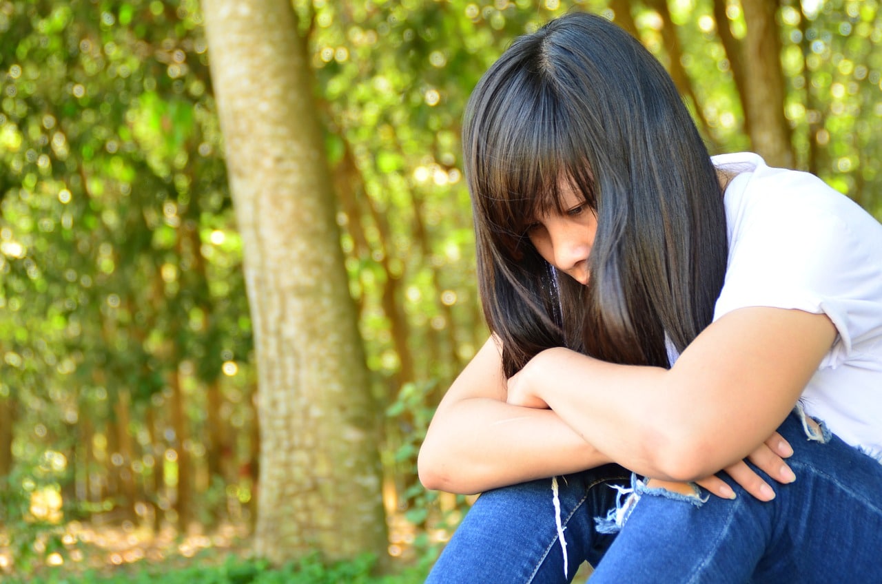 A sad girl exhibiting mental health warnings with her arms folded across her knees