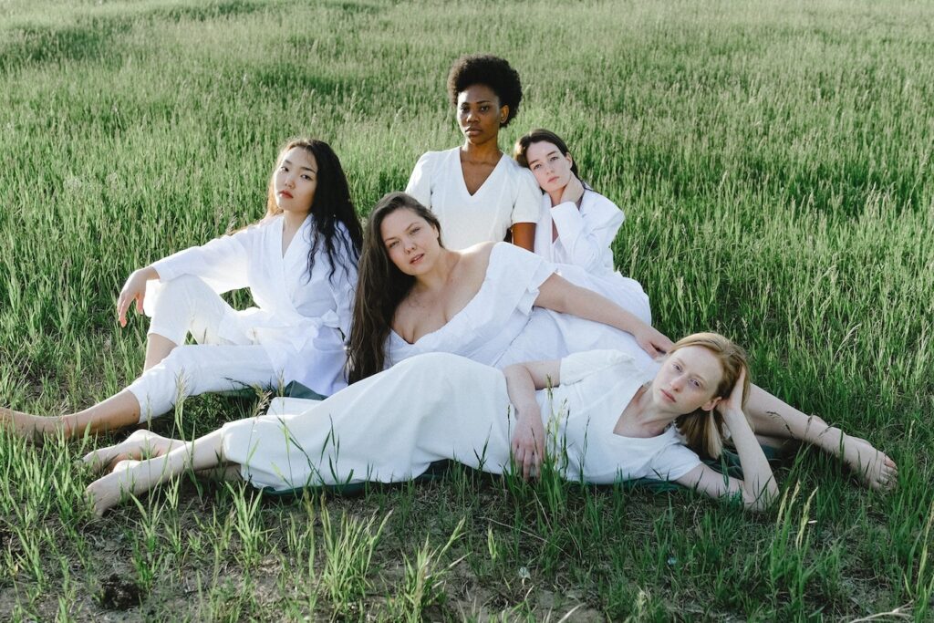 The ladies are all dressed in white on the green grass.