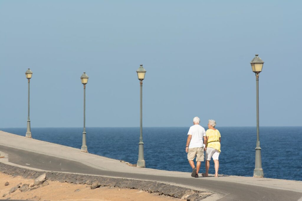 a senior couple walking in the daytime under street lights overlooking the ocean
