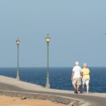a senior couple walking in the daytime under street lights overlooking the ocean