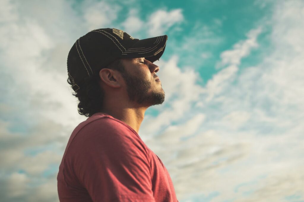 a man wearing a blue cap stairs at the clouds meditating to revitalize your life