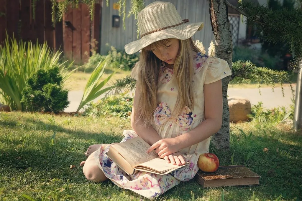 a girl sitting in the shade wearing a straw hat reading a book about the best health