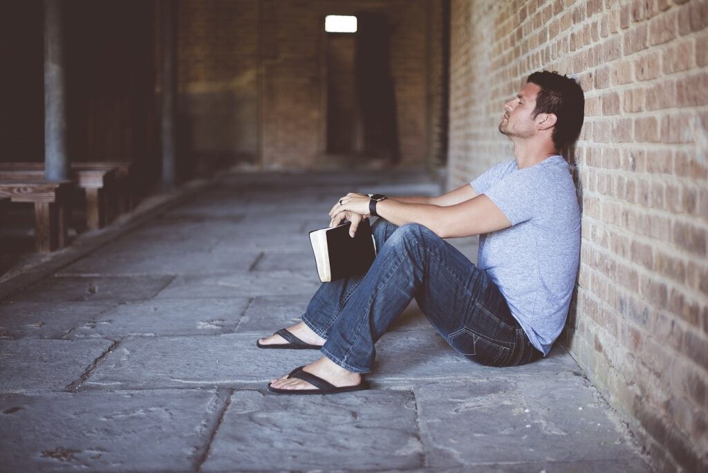 a man sitting on the pavement leaning against the wall holding a book